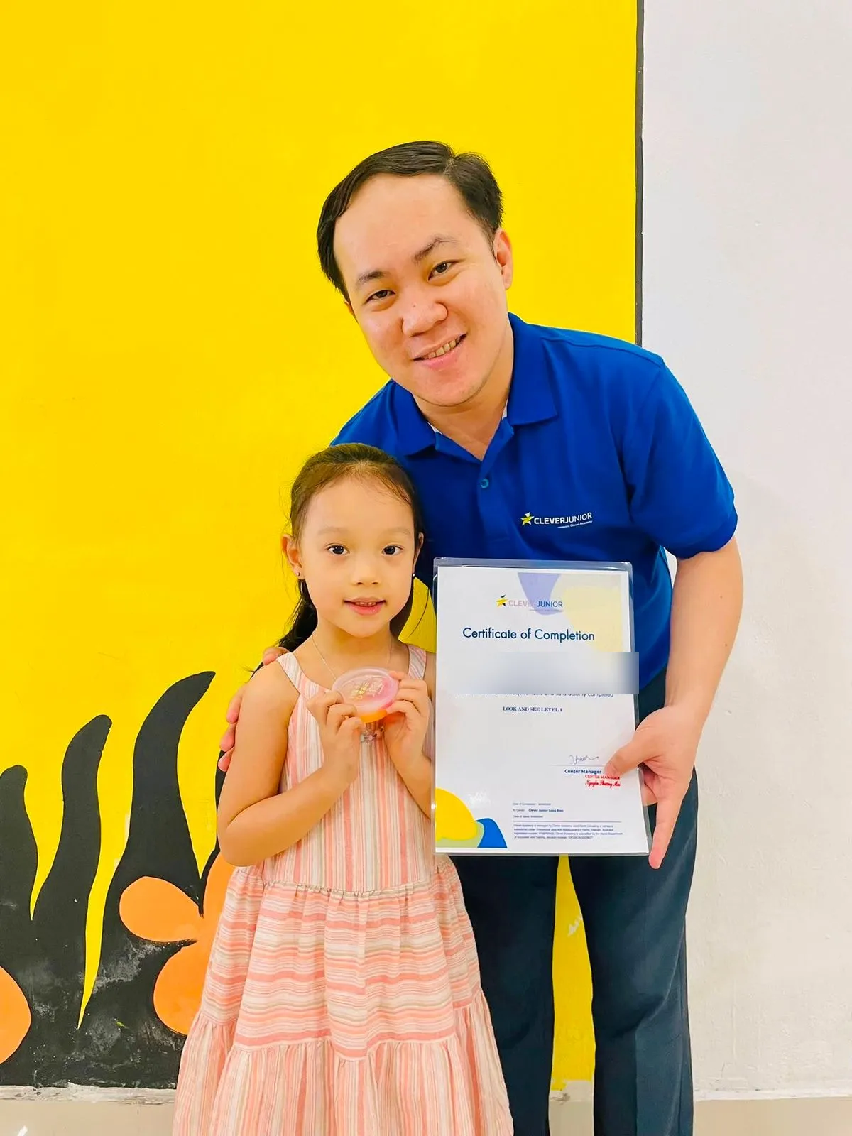 Một bạn nhỏ cười tươi khi nhận chứng nhận hoàn thành khoá học từ thầy tại Clever Junior Long Biên