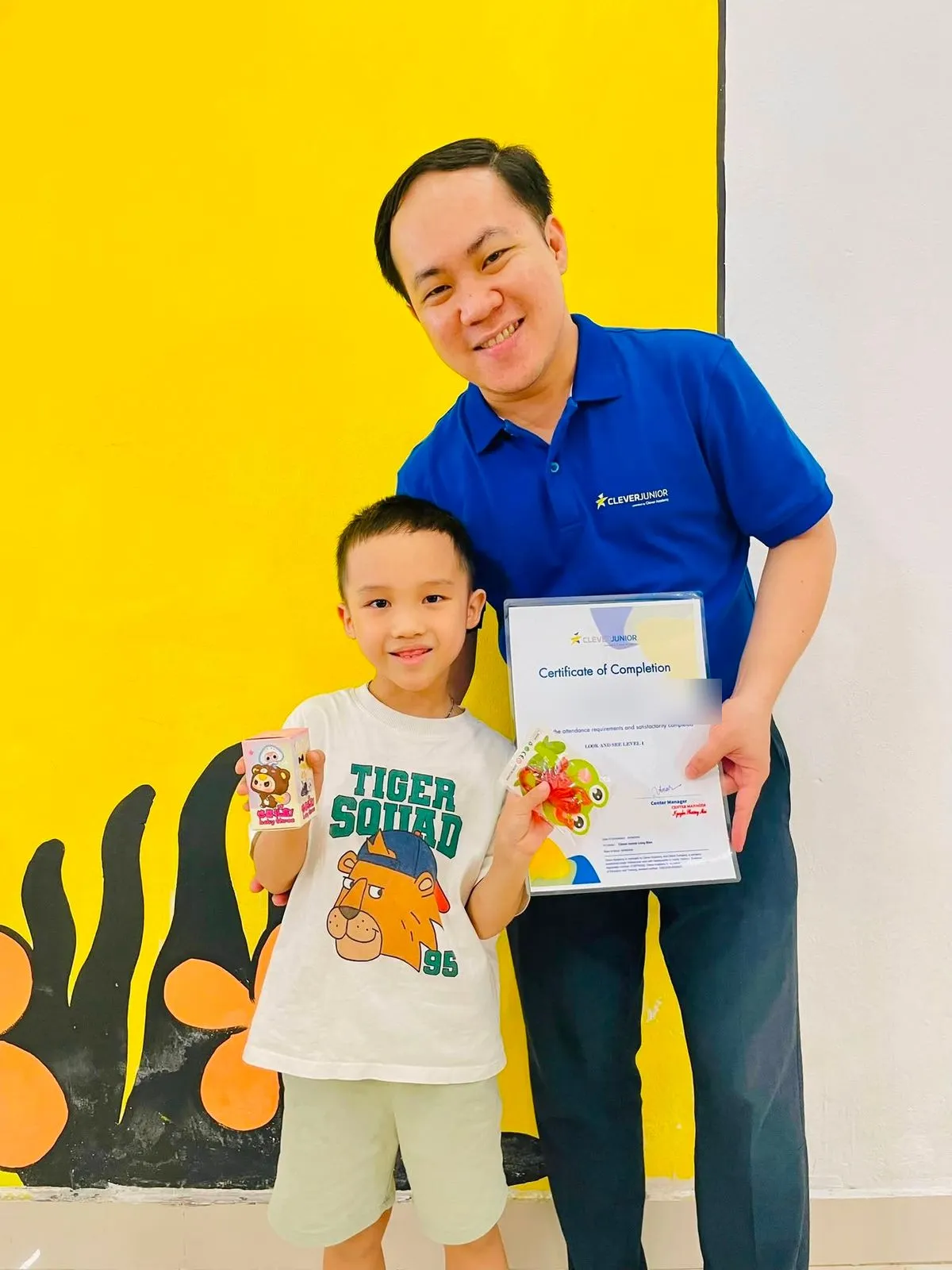 Một bạn nhỏ cầm chứng nhận và phần quà nhỏ trong buổi tổng kết khoá học tại Clever Junior Long Biên