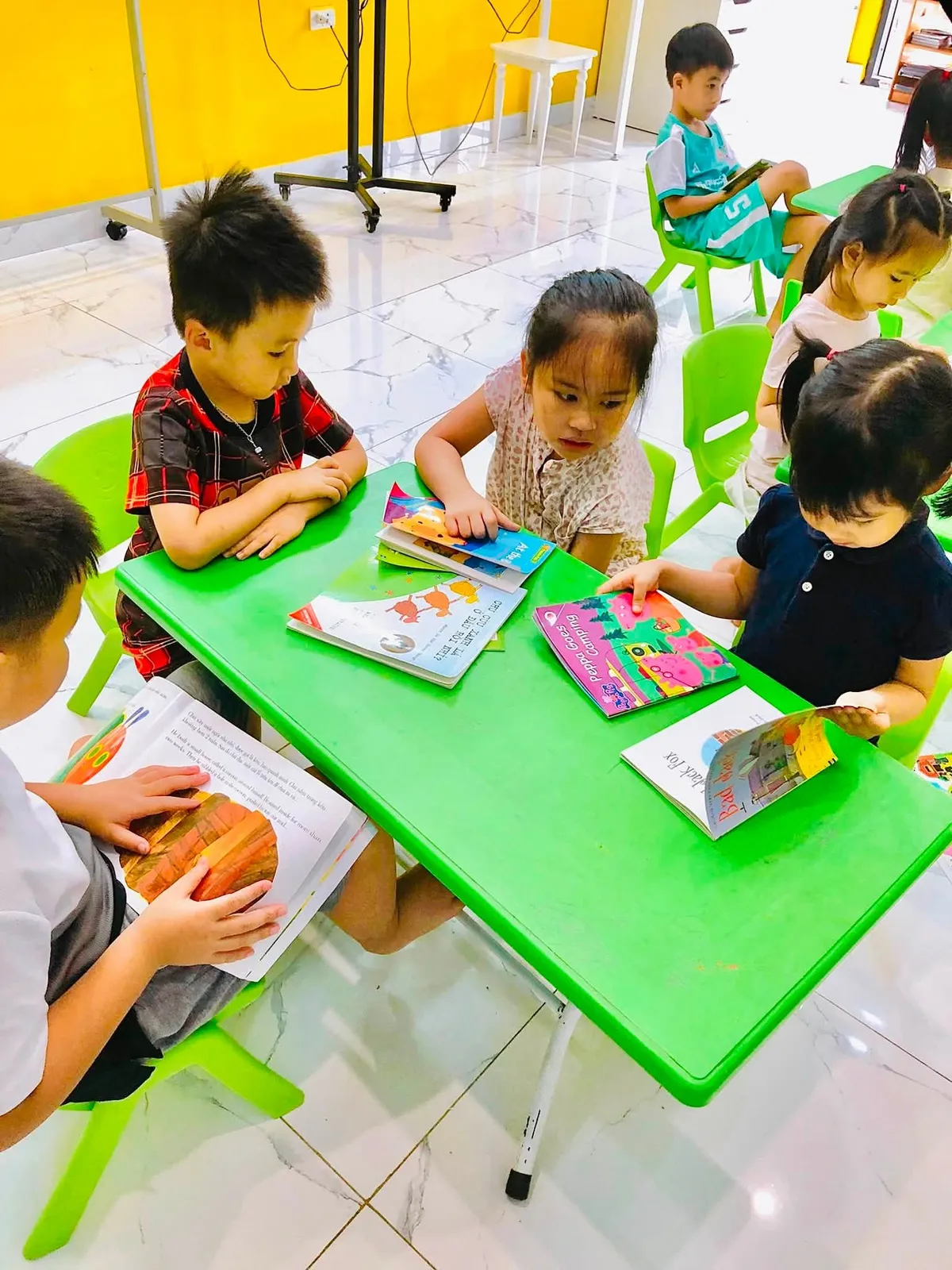 Các bạn nhỏ mỗi người đọc một cuốn sách riêng, trên bàn có cả sách tiếng Anh và sách tiếng Việt