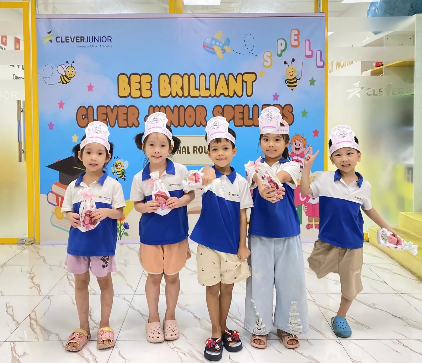 Năm thí sinh nhí mặc đồng phục Clever Junior đứng trước phông nền vòng chung kết Bee Brilliant