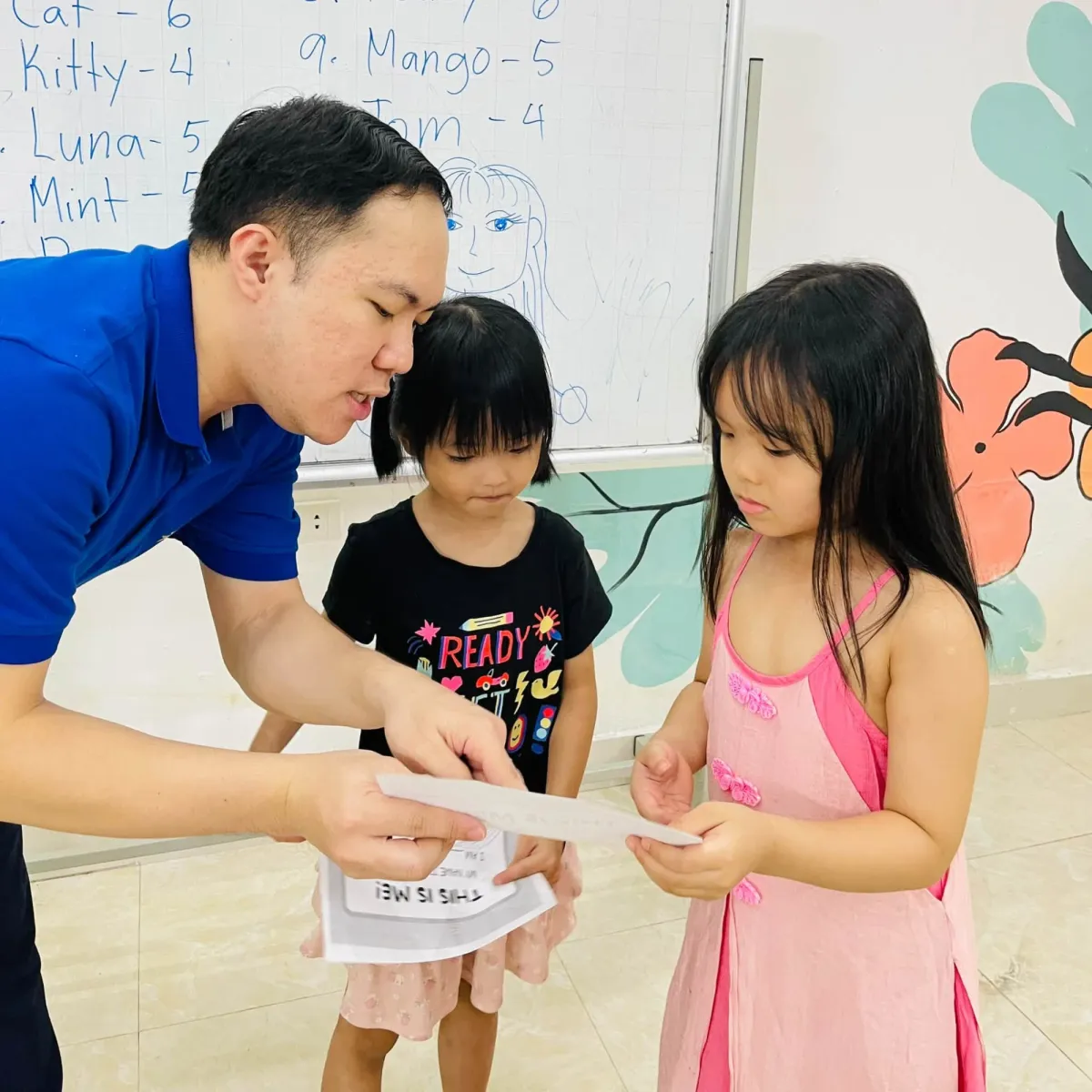 Thầy giáo cùng hai bạn nhỏ xem phiếu bài tập This is me!